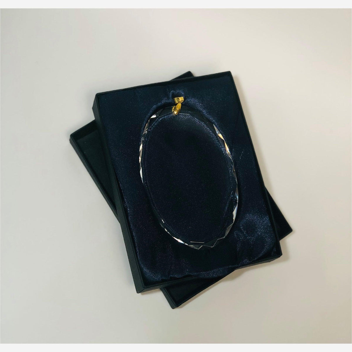 4 inch oval crystal ornament in a black box with navy satin gold clasp hanger